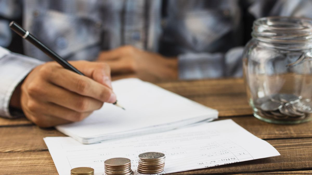 Un hombre hace cuentas, acompañado de un bote con monedas