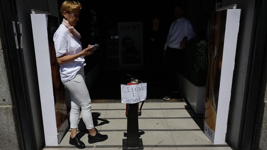 Una mujer revisa su móvil ante una tienda cerrada debido al apagón en un comercio del centro de Madrid, tras el corte de suministro eléctrico que afecta este lunes a España. EFE/Mariscal
