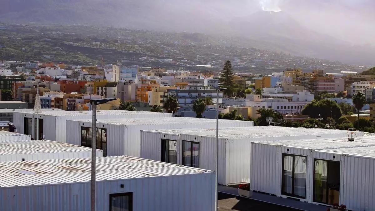 Viviendas en contenedores para personas afectadas por el volcán, que humea detrás, al fondo.