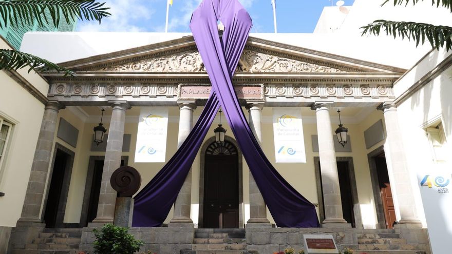 Un lazo violeta cuelga de la fachada del Parlamento canario