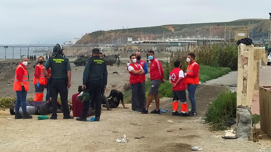 Miembros de la Guardia Civil y de la Cruz Roja atienden a un grupo de inmigrantes marroquí en uno de los espigones fronterizos de Ceuta, donde ayer se batió la cifra récord de llegada de inmigrantes a España en un solo día por vía marítima, contabilizando los 5000 marroquíes que según la delegación del gobierno en Ceuta han llegado a la ciudad autónoma. EFE/Reduan