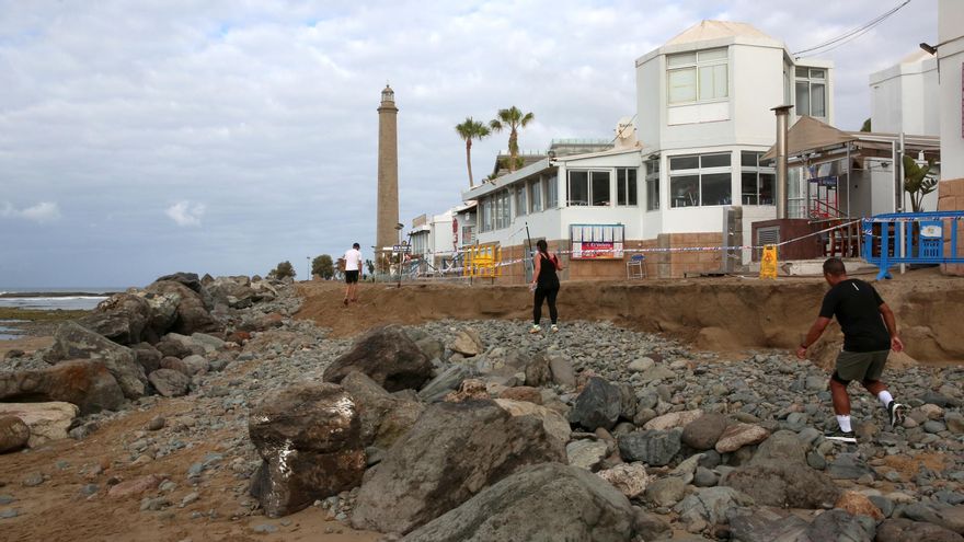 Varias personas transitan por las piedras de la escollera ubicada frente al centro comercial Oasis después de la retirada de un tramo de la pasarela.