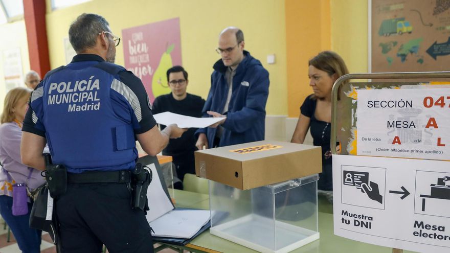 Un policía municipal de Madrid entrega documentación electoral en una de las mesas antes de la apertura de un colegio electoral en Madrid.