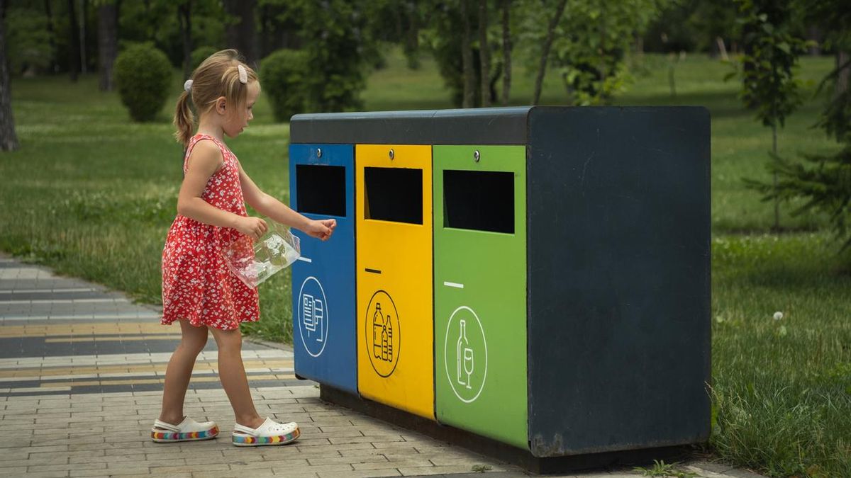 Una niña tira un envase de plástico en una papelera amarilla