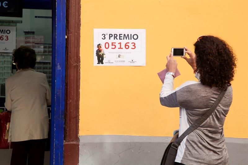 Una mujer fotografía el cartel que acredita que un tercer premio del sorteo de la Lotería de Navidad ha sido vendido en la administración número 9 de Santa Cruz de Tenerife