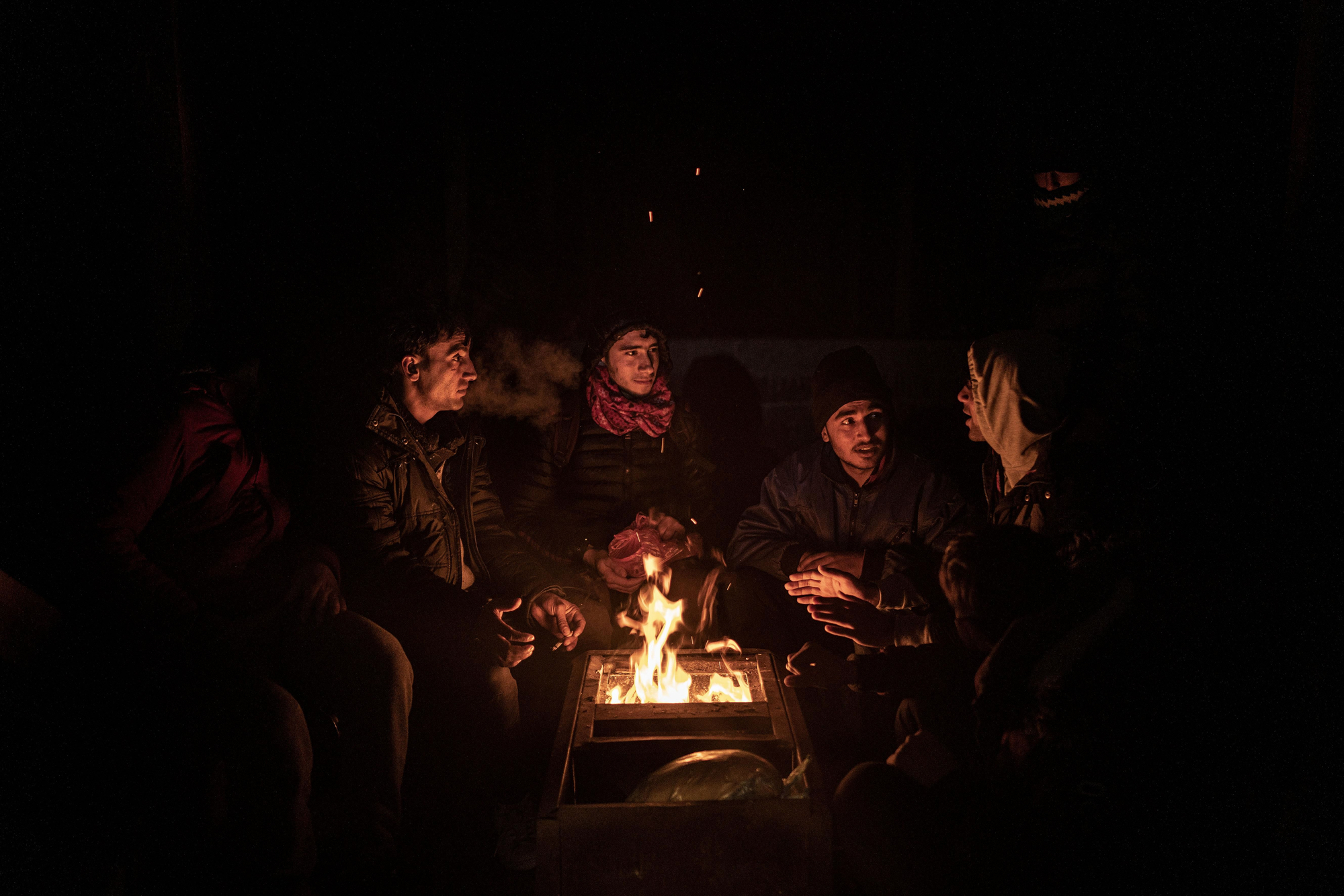 Un grupo de jóvenes afganos, algunos menores de edad, se calientan junto a un fuego en un refugio de montaña la noche antes de cruzar la frontera con Croacia