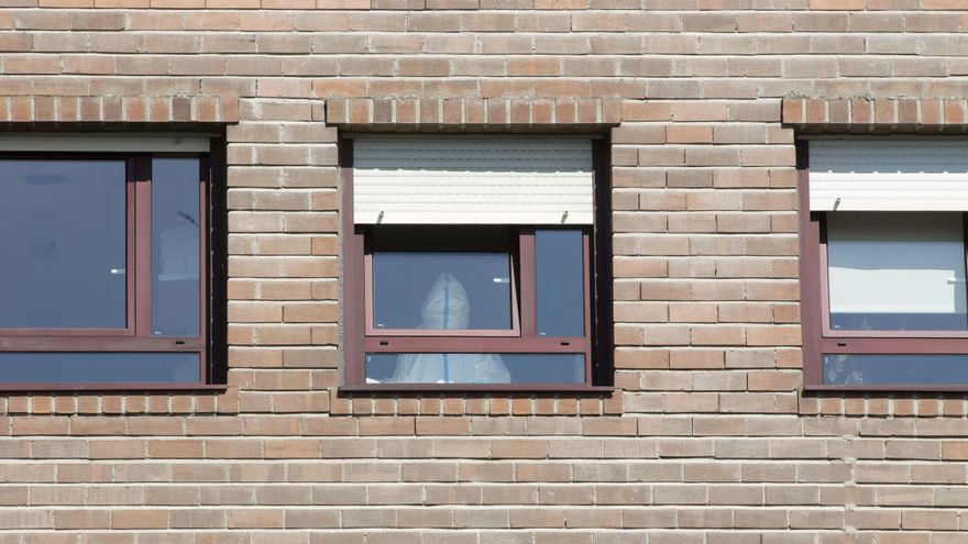 Un trabajador sanitario con un EPI, en la ventana de una habitación de una residencia
