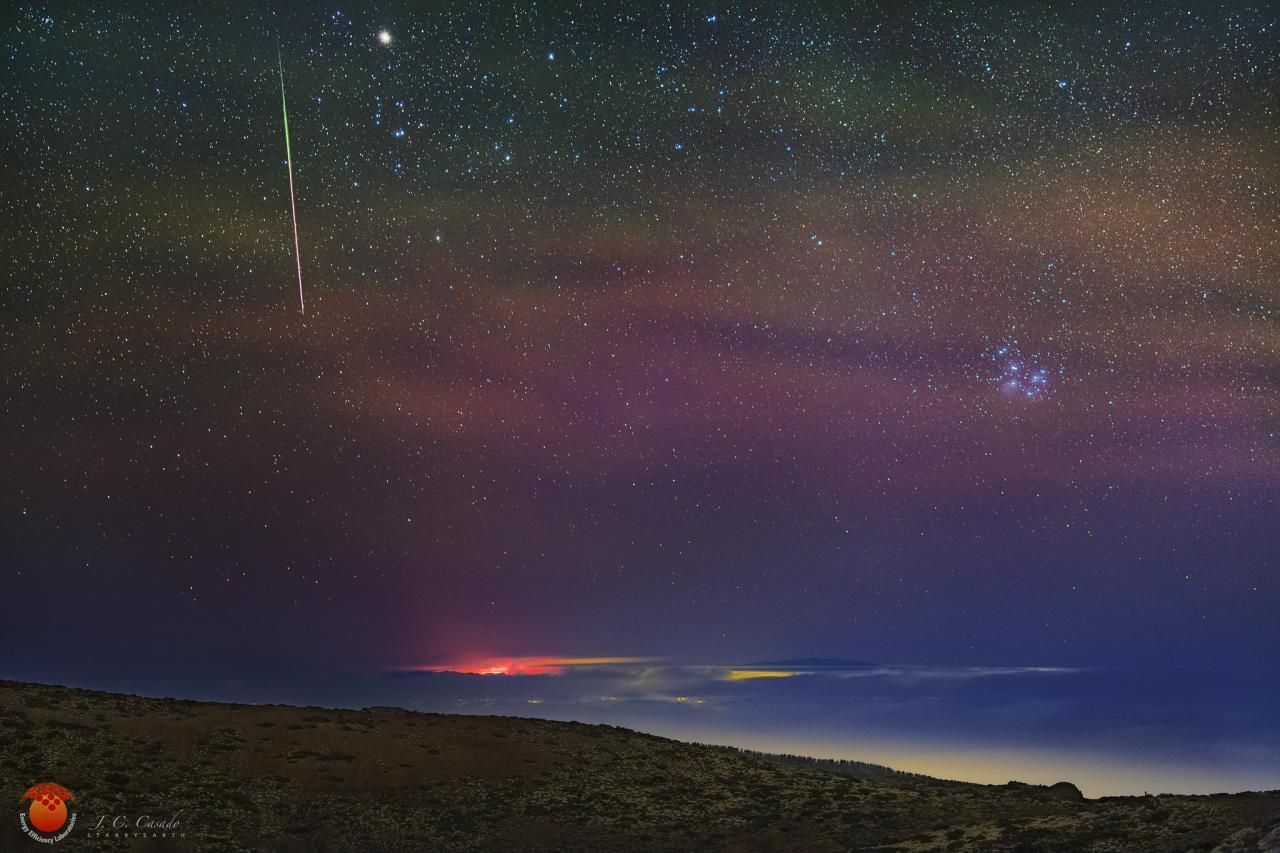 Brillante y colorida Gemínida sobre el volcán de La Palma, la madrugada del 12 de diciembre de 2021. En el cielo, airglow verde y rojo. En la parte superior de la imagen se distingue la estrella Aldebaran (alfa Tauri) y el cúmulo estelar de las Hyades; y a la derecha el cúmulo de Las Pléyades. Crédito: Juan Carlos Casado (starryearth).