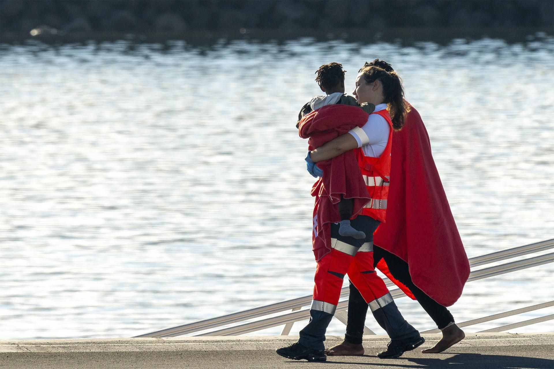 Una treballadora de la Creu Roja porta en braços un nadó arribat a bord d'una pastera
