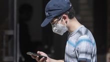 Un joven con mascarilla mira su teléfono móvil.