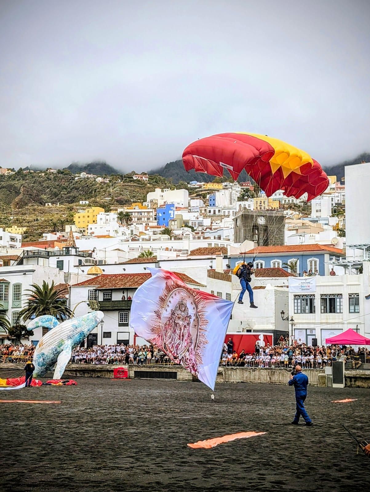 En la imagen, uno de los paracaidistas, en el marco de la  exhibición aérea de la Patrulla Acrobática de Paracaidismo 
 descendiendo hasta la playa de Santa Cruz de La Palma portando una bandera con la imagen de la Virgen de Las Nieves.