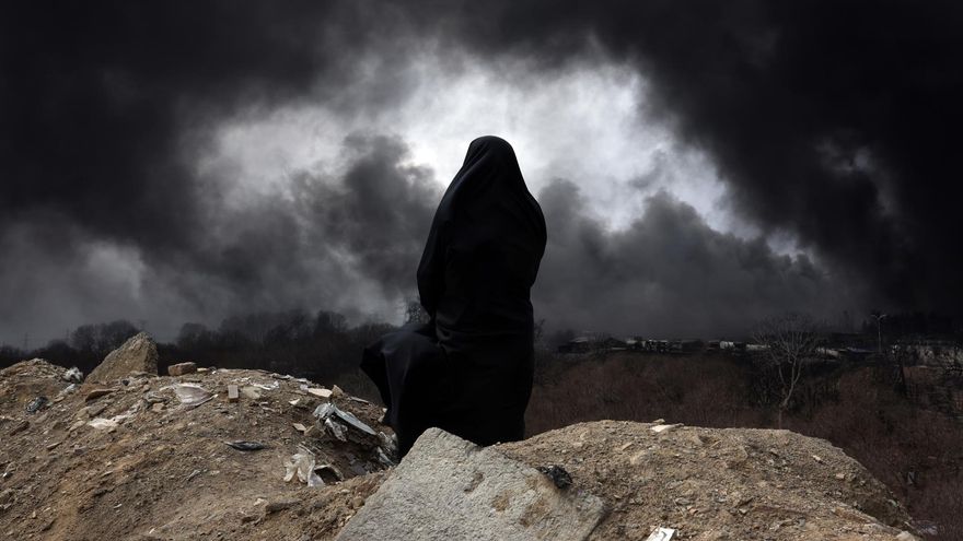Una mujer iraní con velo, miembro de la Media Luna Roja de Irán, observa mientras el humo sigue elevándose desde la refinería de petróleo de Shahran tras el ataque aéreo de anoche en Teherán.