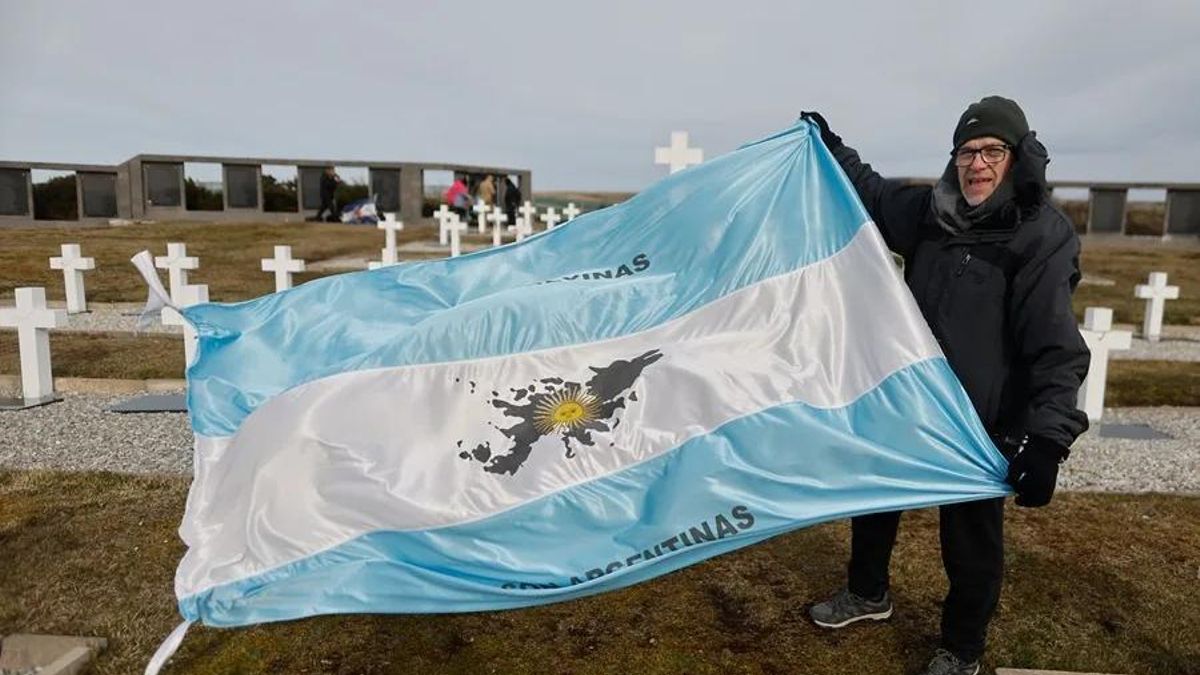 Un excombatiente de Malvinas sostiene un bandera de Argentina en el Cementerio de Darwin, en Islas Malvinas.