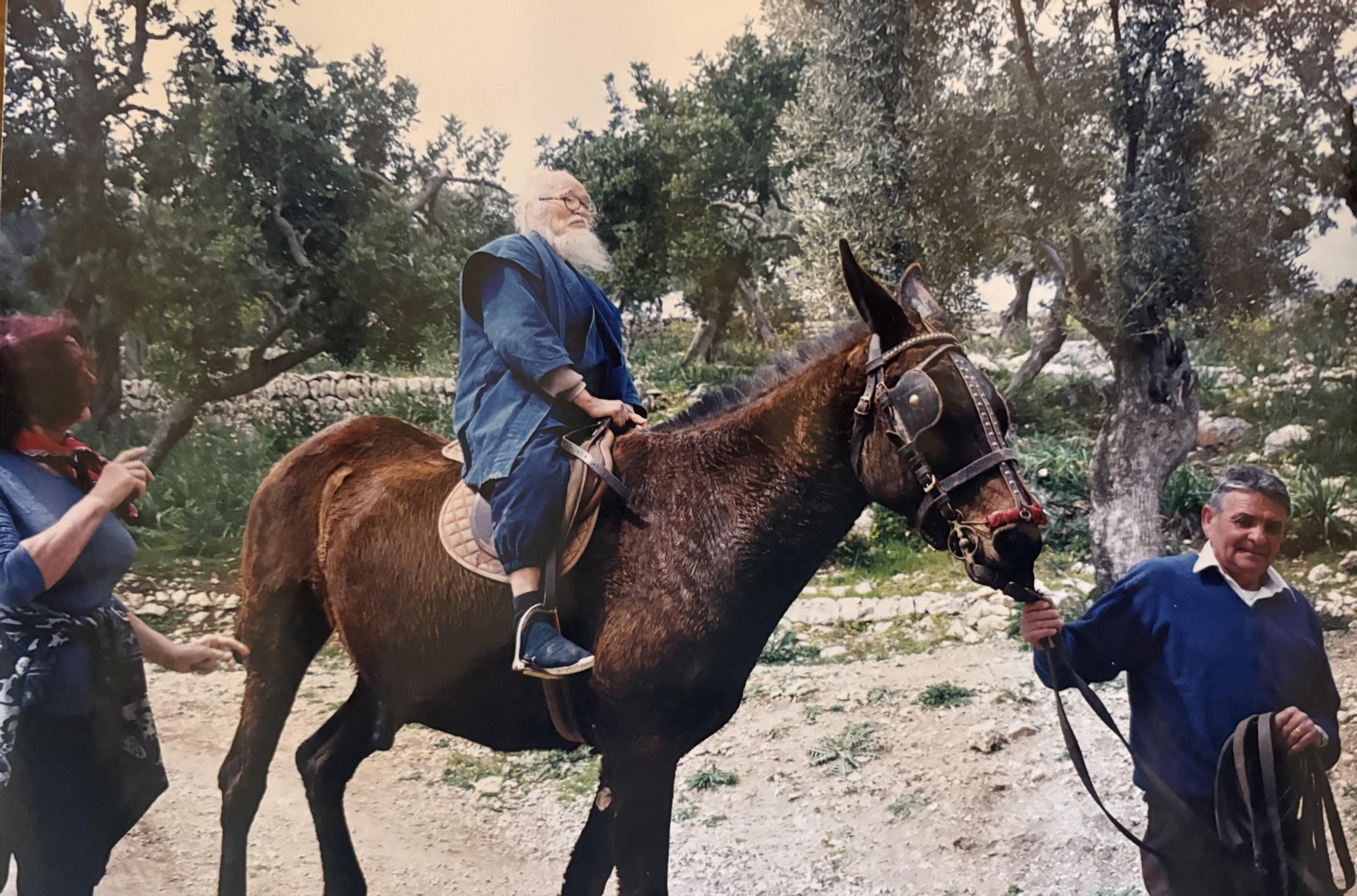 Masanobu Fukuoka recorre el campo mallorquín montado en un mulo, acompañado por vecinos de la zona durante una de sus visitas sobre el terreno en 1999